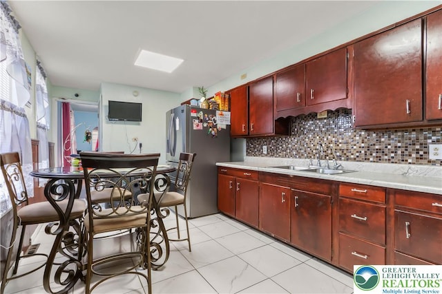 kitchen featuring a sink, decorative backsplash, freestanding refrigerator, and light countertops