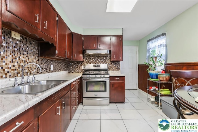 kitchen with a sink, light countertops, under cabinet range hood, and stainless steel gas stove