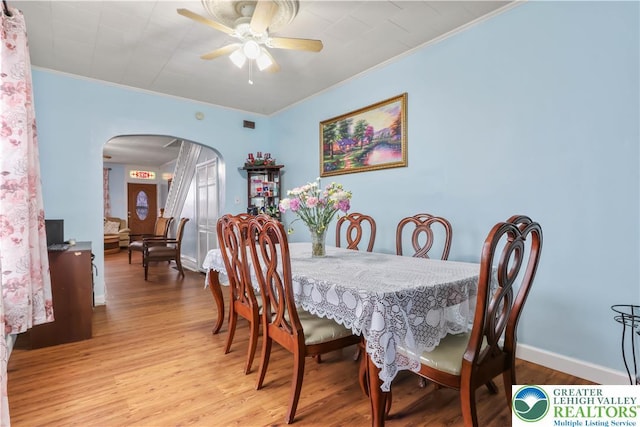 dining room with crown molding, ceiling fan, arched walkways, baseboards, and wood finished floors
