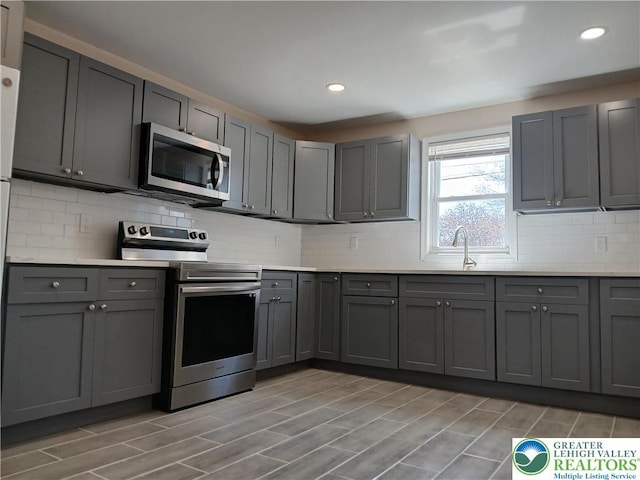 kitchen featuring stainless steel appliances, a sink, gray cabinets, and recessed lighting