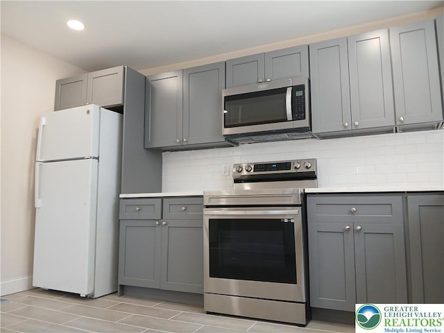 kitchen with light countertops, appliances with stainless steel finishes, gray cabinets, and backsplash