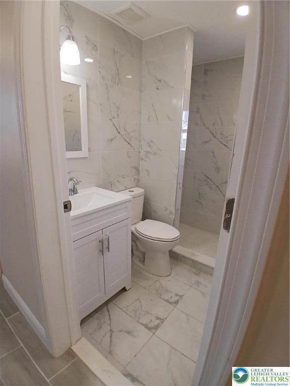 bathroom with toilet, a marble finish shower, marble finish floor, and vanity