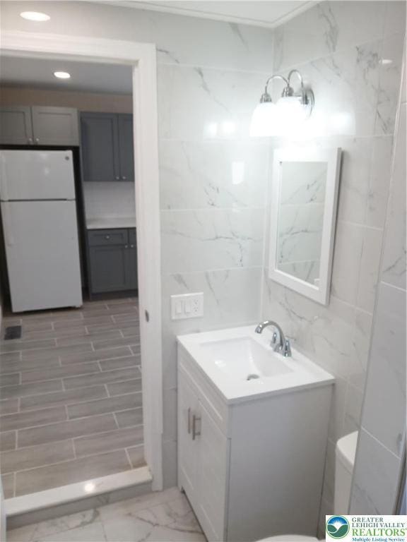 bathroom with vanity, marble finish floor, toilet, and tile walls