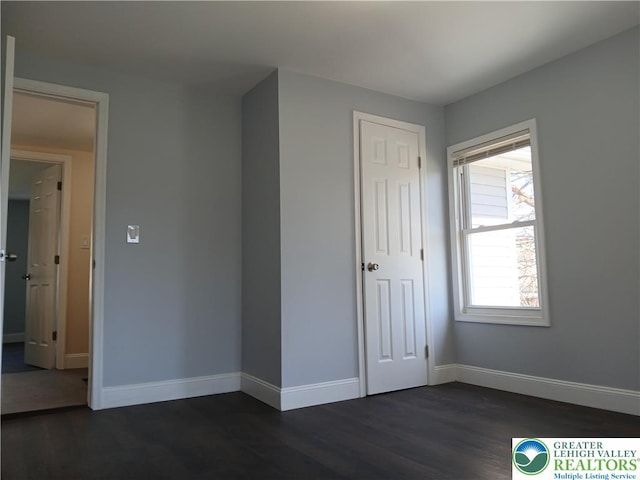 unfurnished bedroom with baseboards, dark wood-style floors, and a closet