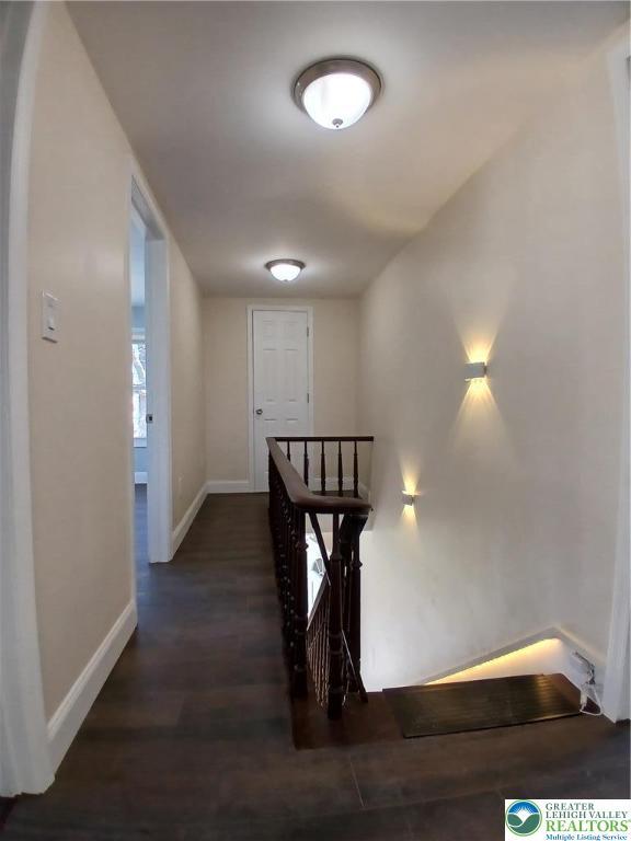 hallway with baseboards, dark wood-type flooring, and an upstairs landing
