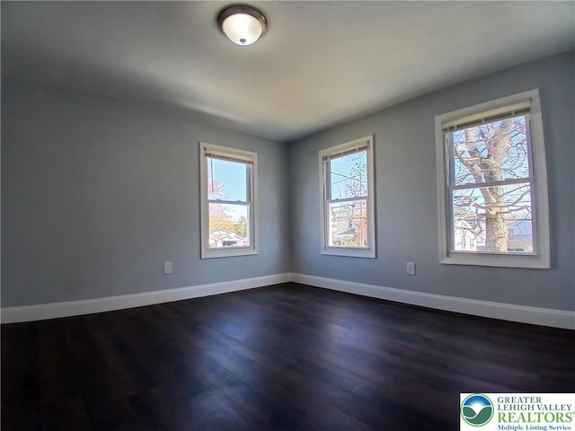 spare room featuring baseboards and dark wood-style floors