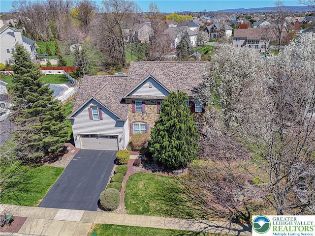 view of front of property featuring an attached garage, a residential view, stone siding, and aphalt driveway