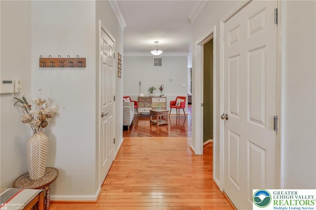 corridor with light wood finished floors, crown molding, and visible vents