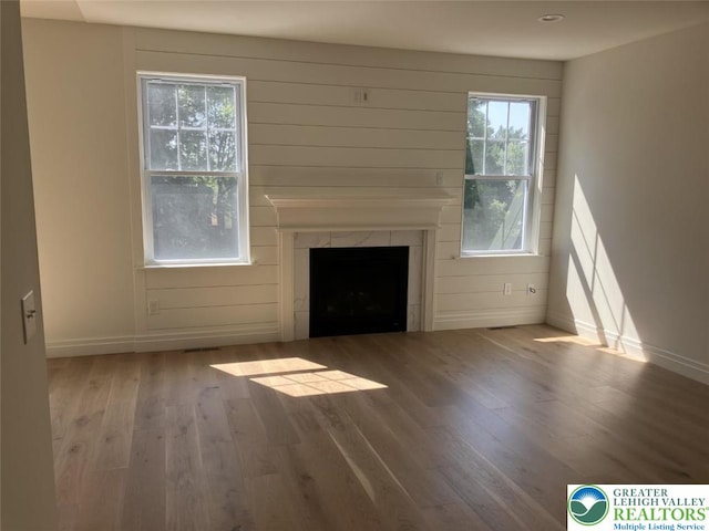 unfurnished living room with a premium fireplace, baseboards, plenty of natural light, and wood finished floors