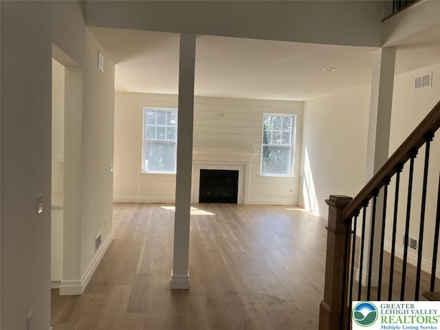 unfurnished living room featuring baseboards, visible vents, a large fireplace, and wood finished floors