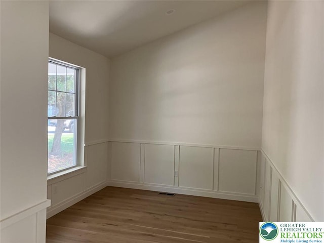 spare room featuring a wainscoted wall, a decorative wall, wood finished floors, and visible vents