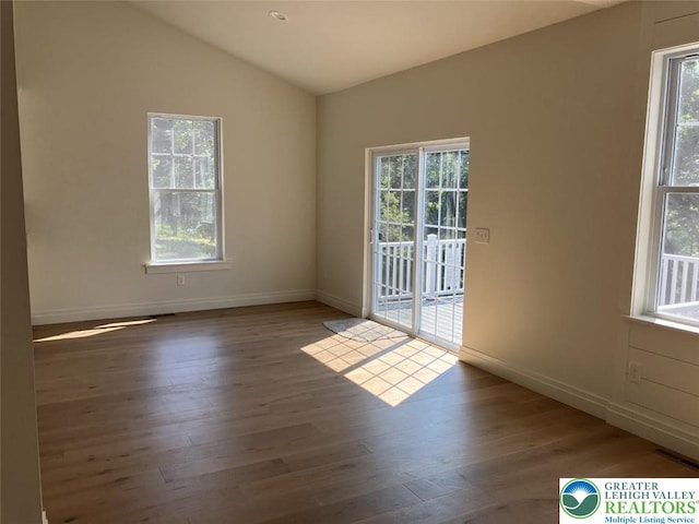 unfurnished room featuring baseboards, lofted ceiling, wood finished floors, and a wealth of natural light