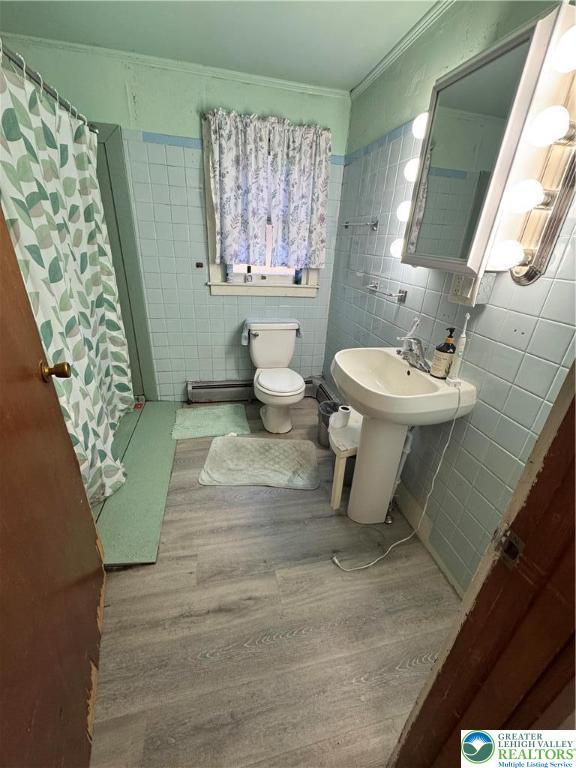 bathroom with ornamental molding, curtained shower, wood finished floors, toilet, and tile walls