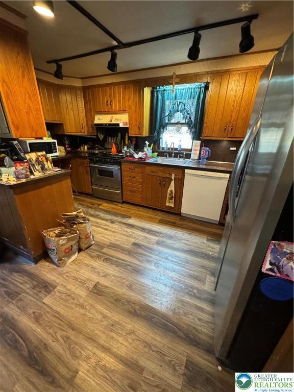 kitchen with dark countertops, brown cabinetry, appliances with stainless steel finishes, and track lighting