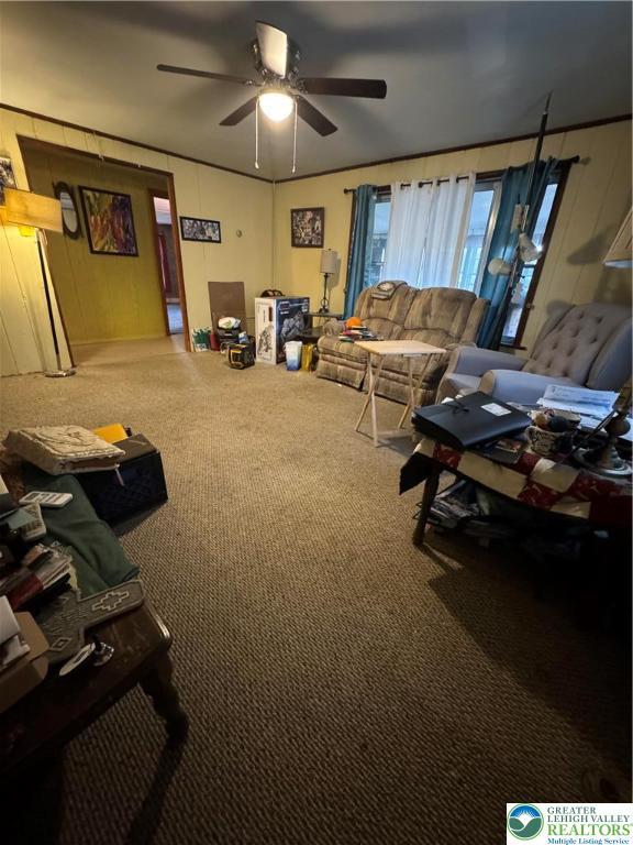 carpeted living room featuring a ceiling fan and wood walls