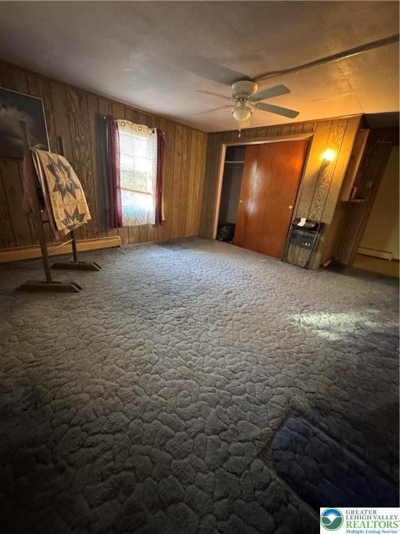 unfurnished bedroom with carpet floors, a baseboard heating unit, and wood walls