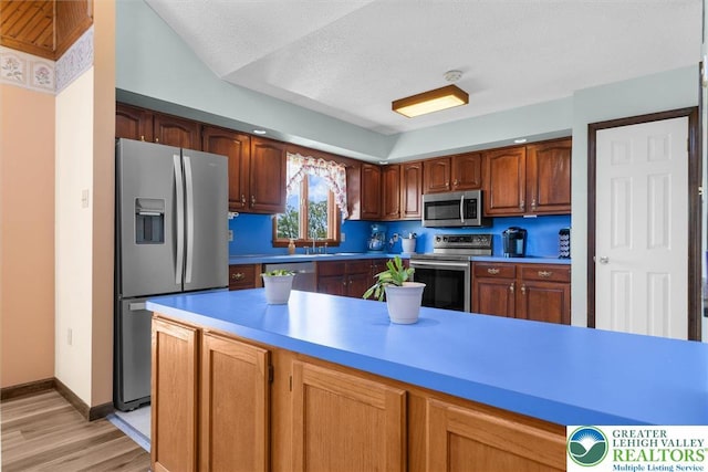 kitchen with baseboards, light countertops, brown cabinets, light wood-style flooring, and appliances with stainless steel finishes