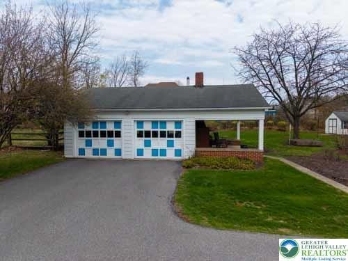 view of front of home with a chimney, a front yard, a garage, an outdoor structure, and aphalt driveway