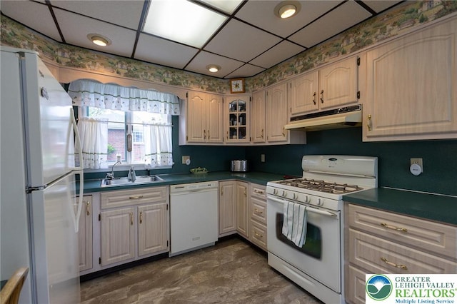 kitchen with dark countertops, a sink, white appliances, a drop ceiling, and under cabinet range hood