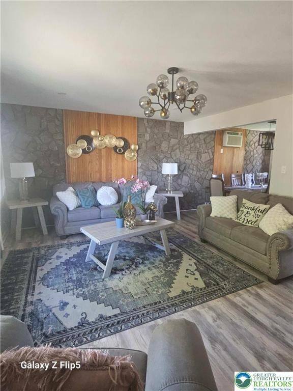 living area featuring a wall unit AC, wood finished floors, and a notable chandelier