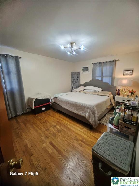 bedroom featuring a chandelier, wood finished floors, and a wall mounted air conditioner