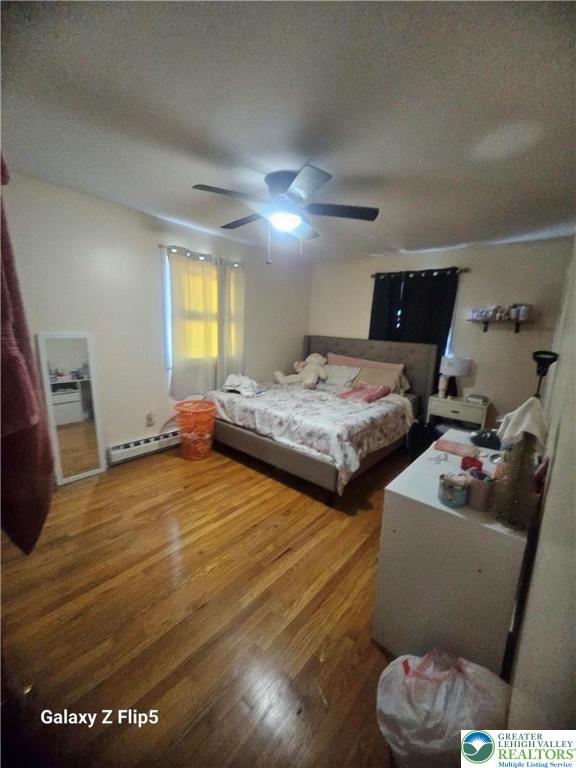 bedroom with ceiling fan, a baseboard heating unit, and wood finished floors