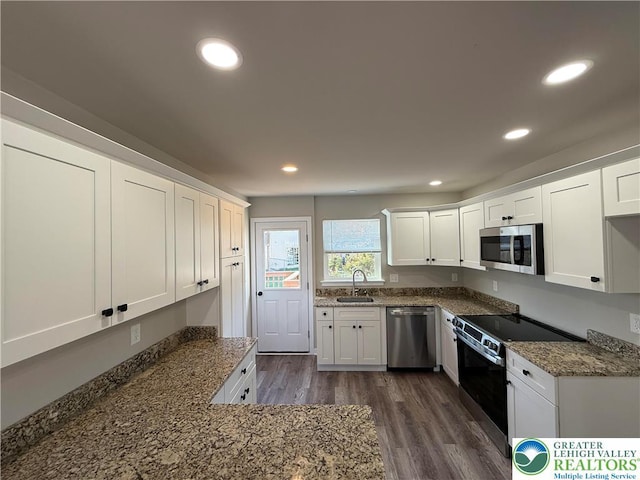 kitchen with a sink, dark stone counters, stainless steel appliances, and dark wood-style flooring