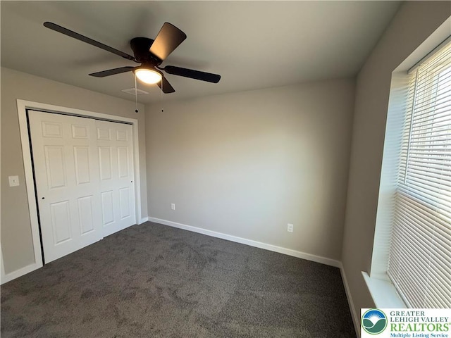 unfurnished bedroom with visible vents, a closet, baseboards, dark colored carpet, and a ceiling fan