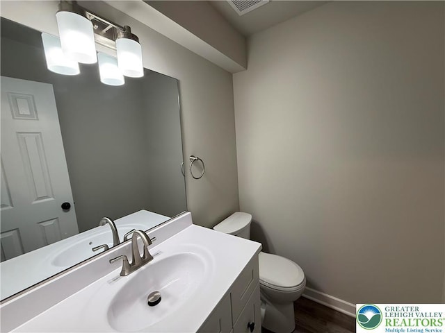 half bath with vanity, toilet, baseboards, wood finished floors, and visible vents