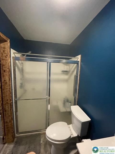 full bath featuring toilet, vaulted ceiling, wood finished floors, and a stall shower