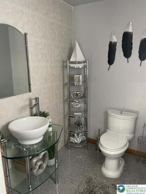 bathroom featuring a sink, tile walls, baseboards, and toilet