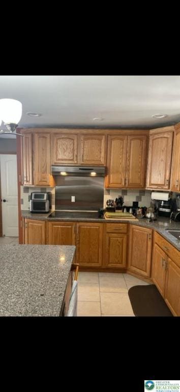 kitchen featuring under cabinet range hood, black electric cooktop, and light tile patterned floors