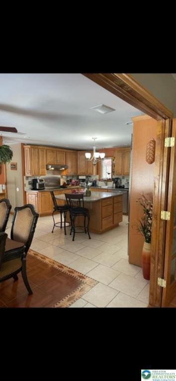 kitchen with brown cabinetry, under cabinet range hood, light tile patterned flooring, and a kitchen bar