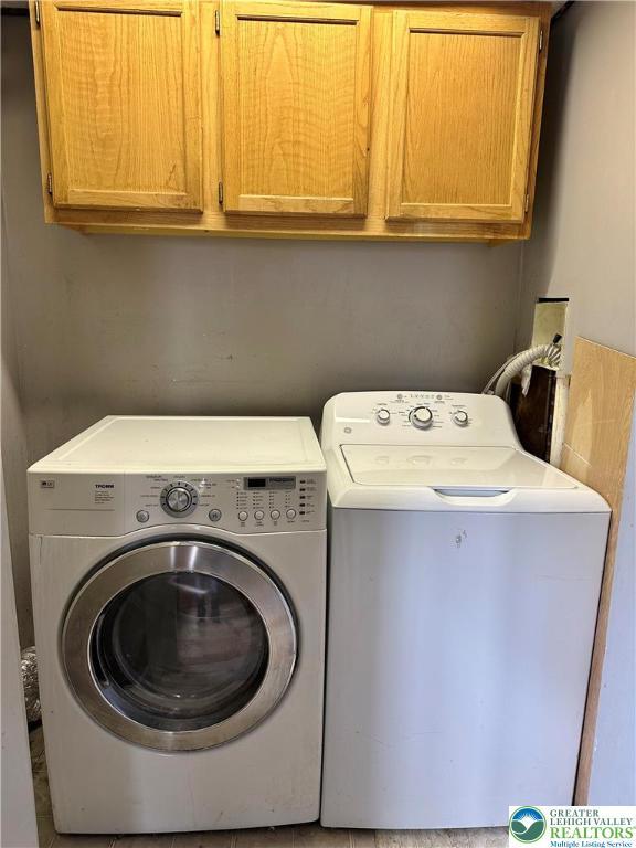 clothes washing area with separate washer and dryer and cabinet space