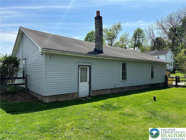 rear view of property with a yard, fence, and a chimney