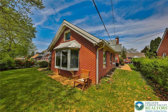 view of side of property featuring a lawn, a chimney, and brick siding