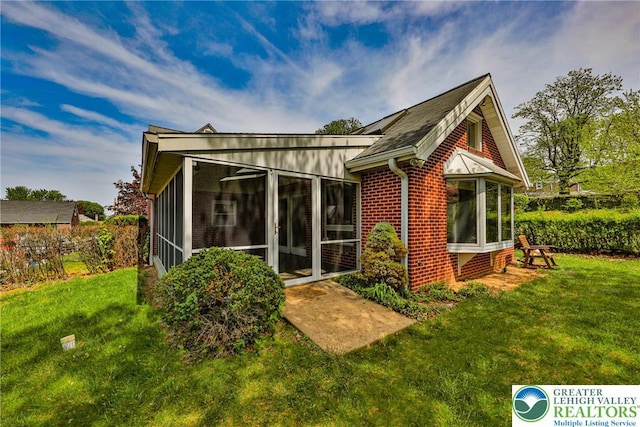 back of house featuring a lawn, brick siding, and a sunroom