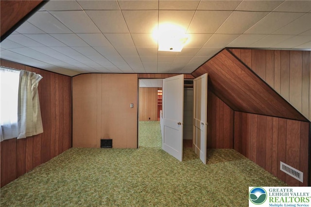 additional living space with visible vents, wood walls, carpet flooring, and vaulted ceiling