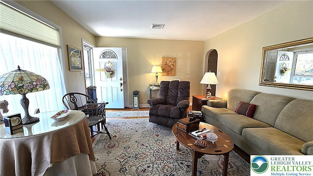 living room featuring arched walkways, visible vents, a healthy amount of sunlight, and wood finished floors
