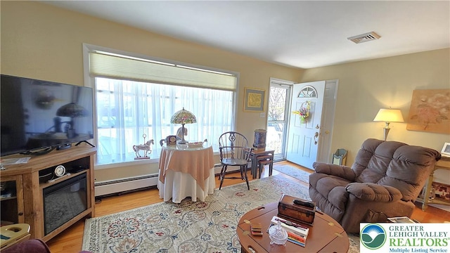 living room with light wood-style floors, baseboard heating, and visible vents
