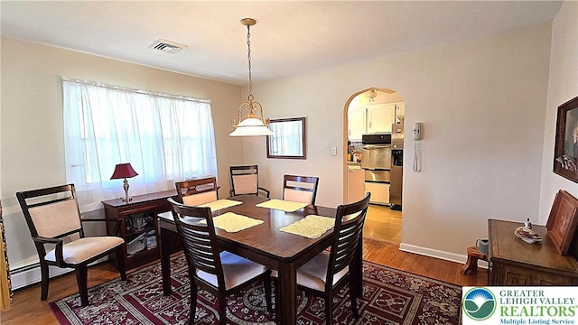 dining space featuring visible vents, arched walkways, baseboards, and wood finished floors