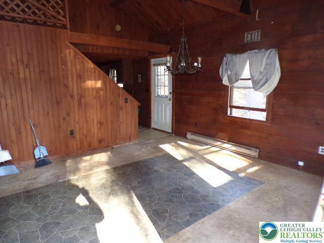 interior space with stone flooring, wooden walls, baseboard heating, vaulted ceiling with beams, and a chandelier