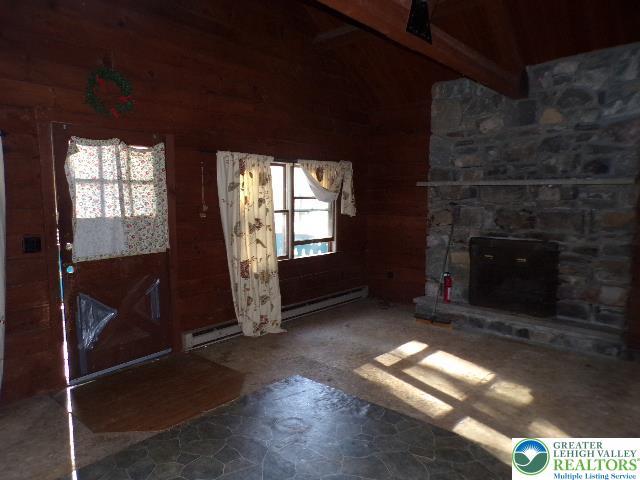 interior space featuring plenty of natural light, lofted ceiling with beams, a baseboard heating unit, and wooden walls