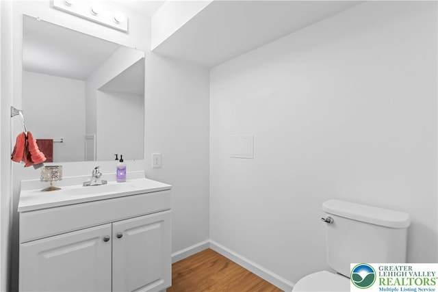 half bath with toilet, baseboards, wood finished floors, and vanity