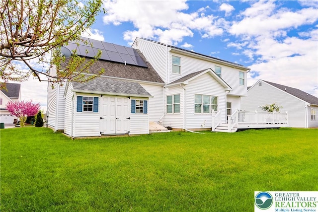 rear view of house featuring a lawn, a shingled roof, solar panels, and a deck