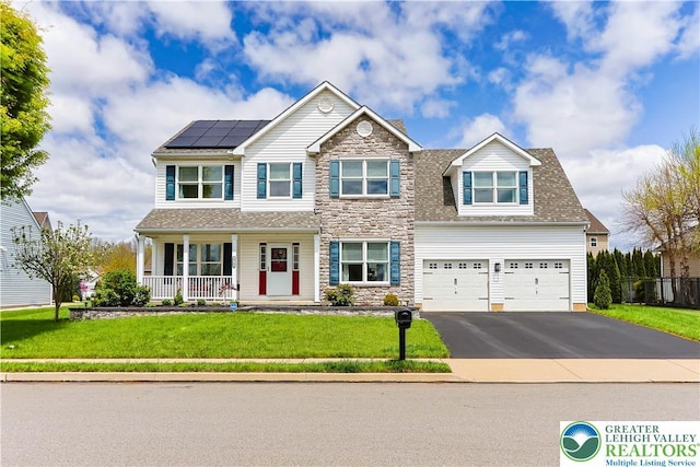 craftsman-style house with a porch, a front yard, roof mounted solar panels, aphalt driveway, and stone siding