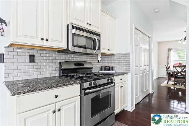kitchen featuring a wainscoted wall, white cabinets, tasteful backsplash, dark stone countertops, and appliances with stainless steel finishes