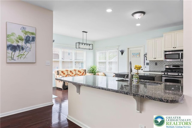 kitchen with dark stone counters, appliances with stainless steel finishes, a kitchen breakfast bar, and dark wood-type flooring
