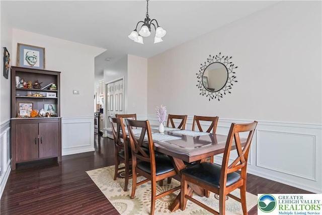 dining space with an inviting chandelier, dark wood finished floors, a decorative wall, and a wainscoted wall