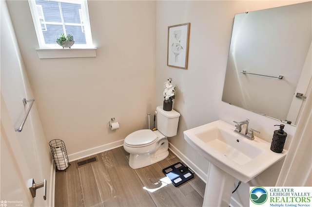 half bath featuring baseboards, toilet, wood finished floors, and visible vents